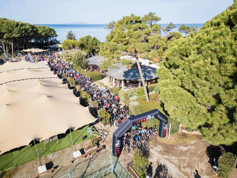 L'arco di partenza di Unpaved Roads nella pineta di Punta Ala, con la folla di ciclisti pronti a partire, visto dall'alto