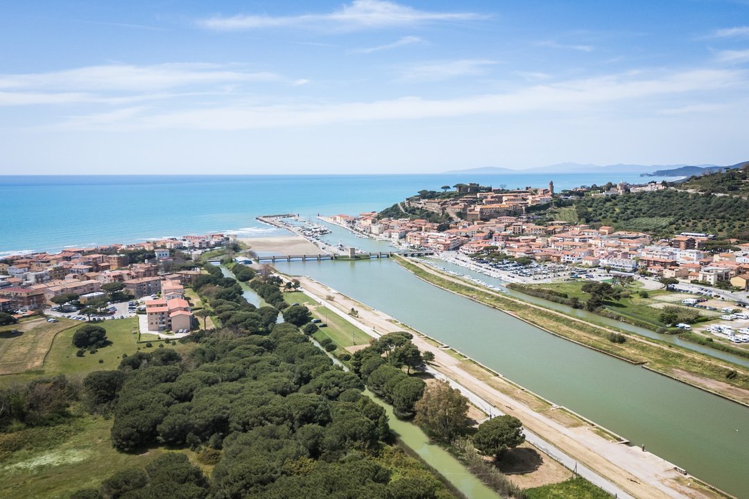 Veduta aerea di una città costiera con un fiume che sfocia nel mare, circondata da colline e vegetazione.